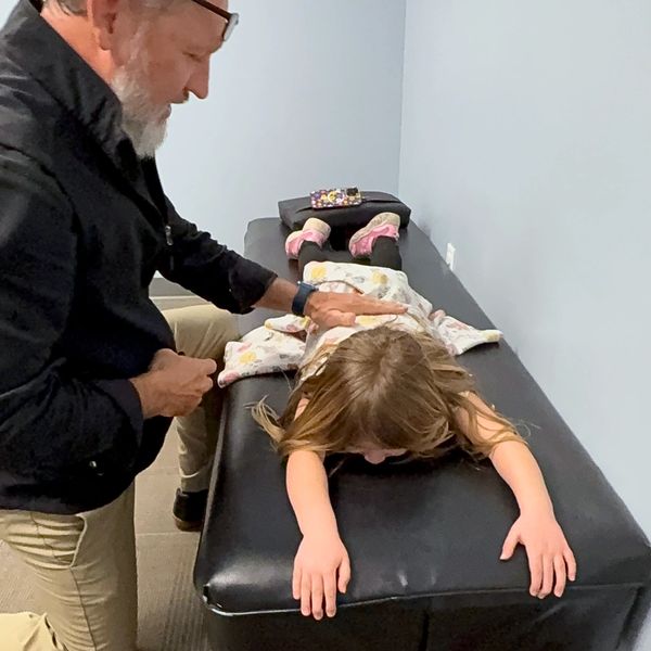 Man examines young girl lying face down on medical table.