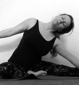 Woman in black tank top doing a seated side stretch yoga pose.
