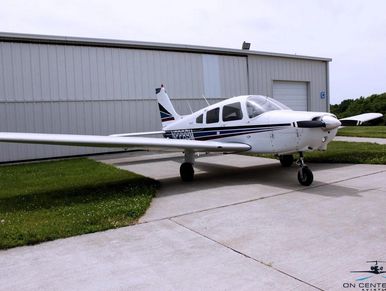 Small white single-engine airplane parked on concrete near a hangar.