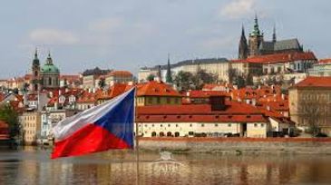 Czech flag waving by the Vltava River with Prague's historic skyline.