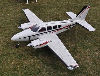 Small twin-engine white airplane parked on grass with red and black stripes.