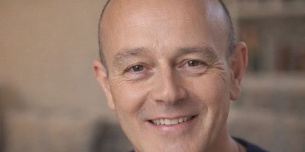 Smiling bald man with a blurred background.