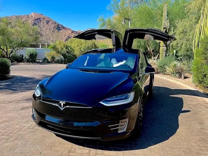 Black Tesla Model X with falcon wing doors open on a sunny day.