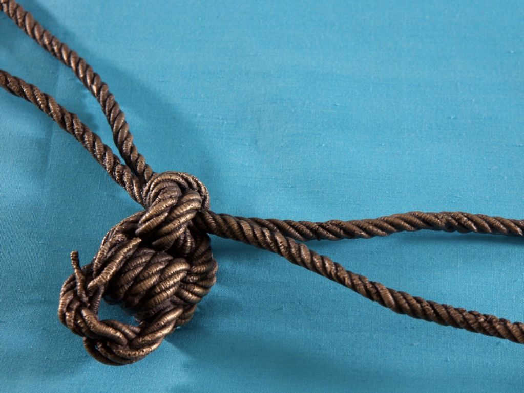 Brown rope tied in a complex knot on blue fabric.