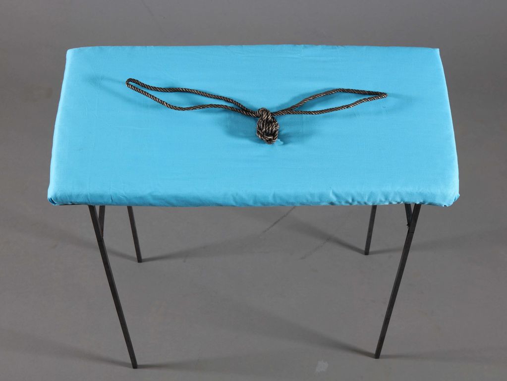 Blue-covered rectangular stool with tied rope on top.