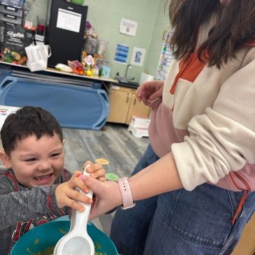 A child happily helps an adult scoop food in a kitchen.