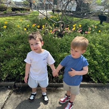 Two young boys holding hands outdoors on a sunny day.