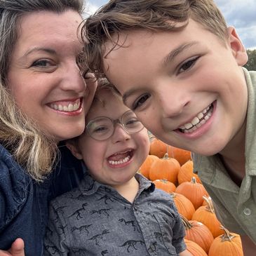A smiling woman and two boys posing with pumpkins outdoors.