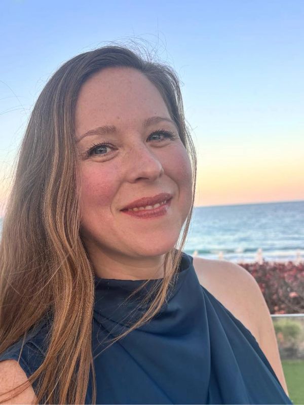 Smiling woman with long hair near the ocean at sunset.