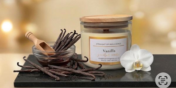 Vanilla-scented candle with vanilla beans and a white orchid on a black surface.