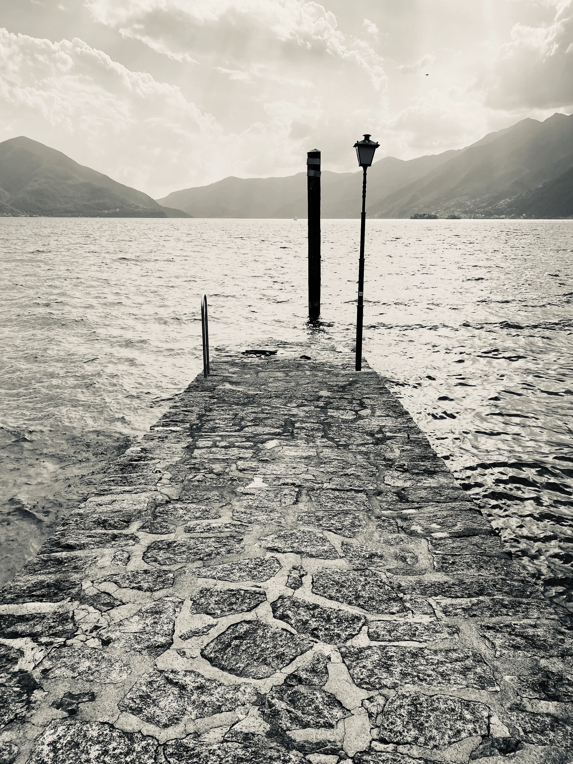 Stone pier extending into a calm lake with mountains in the distance.