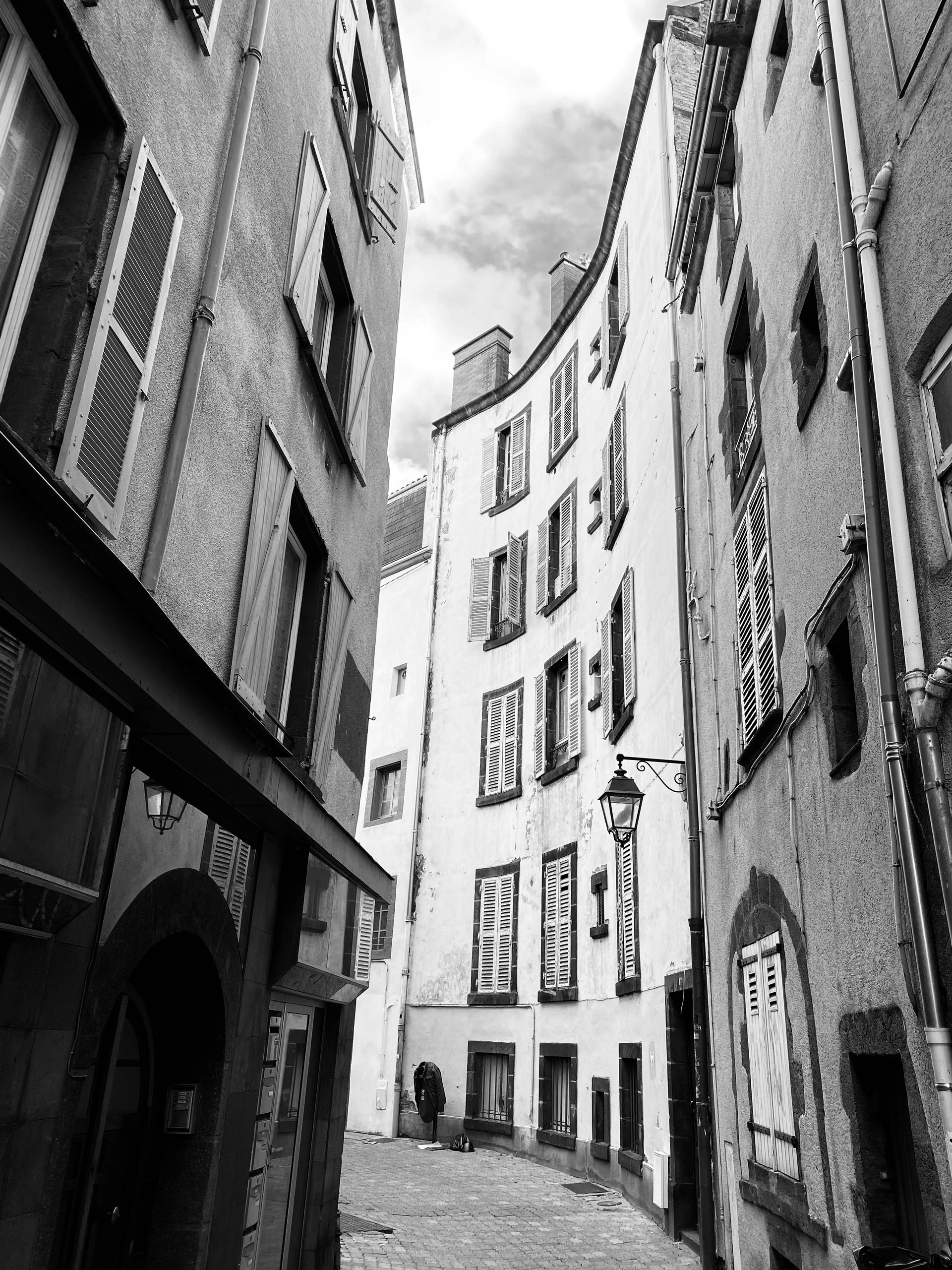 Narrow European street with shuttered windows and cobblestone pavement in black and white.