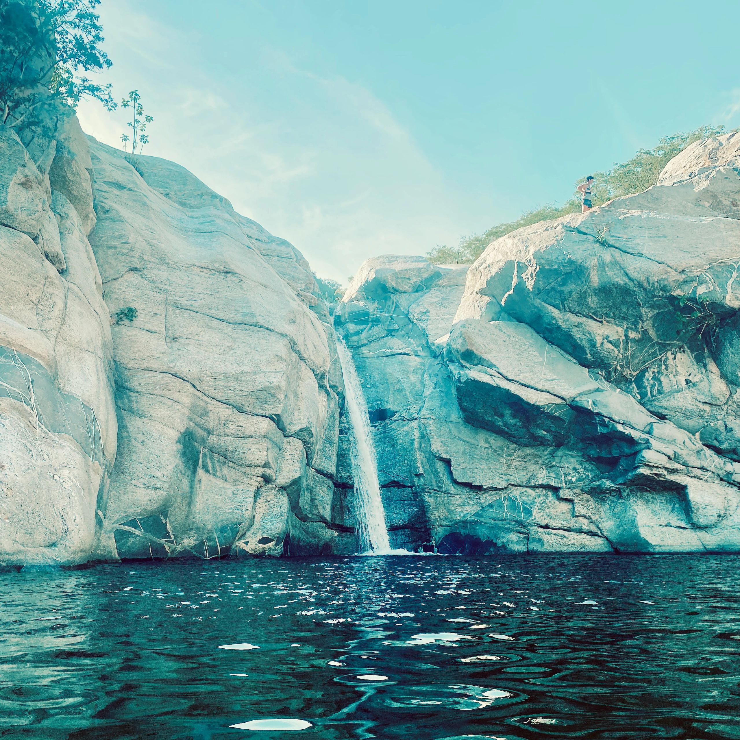 A serene waterfall cascading into a clear pool surrounded by large rocks.
