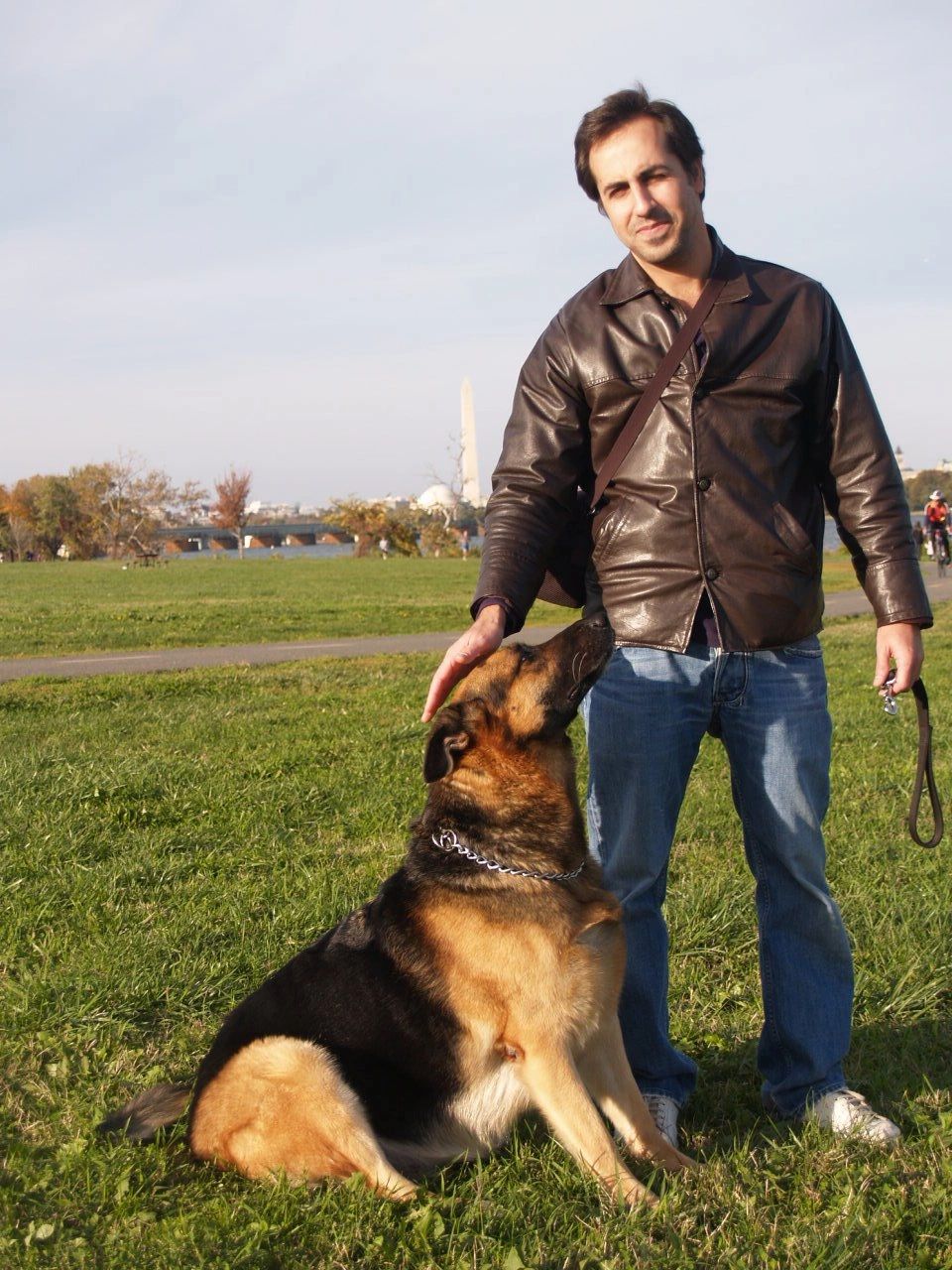 Man petting a German shepherd in a park.