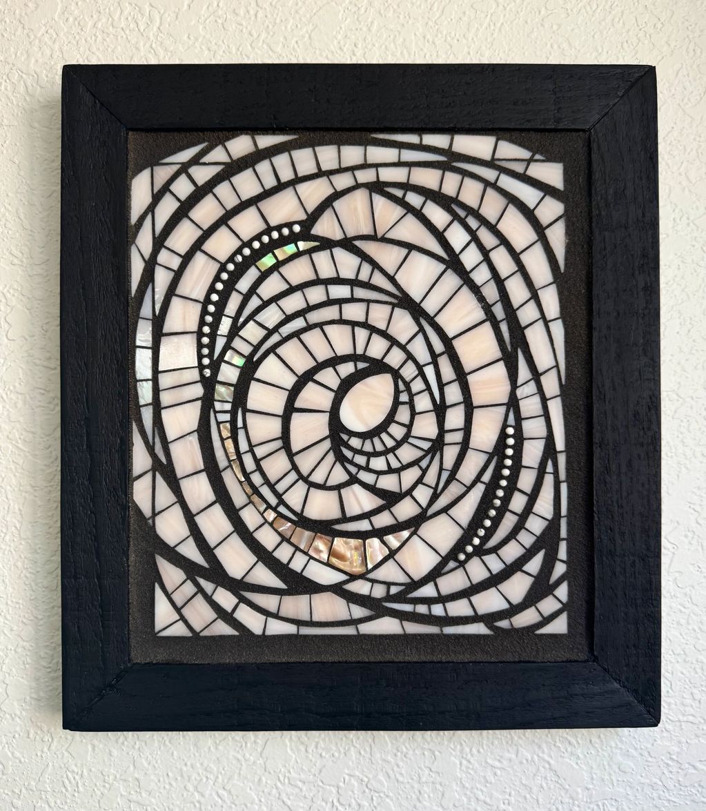 Abstract spiral mosaic art in a black wooden frame.