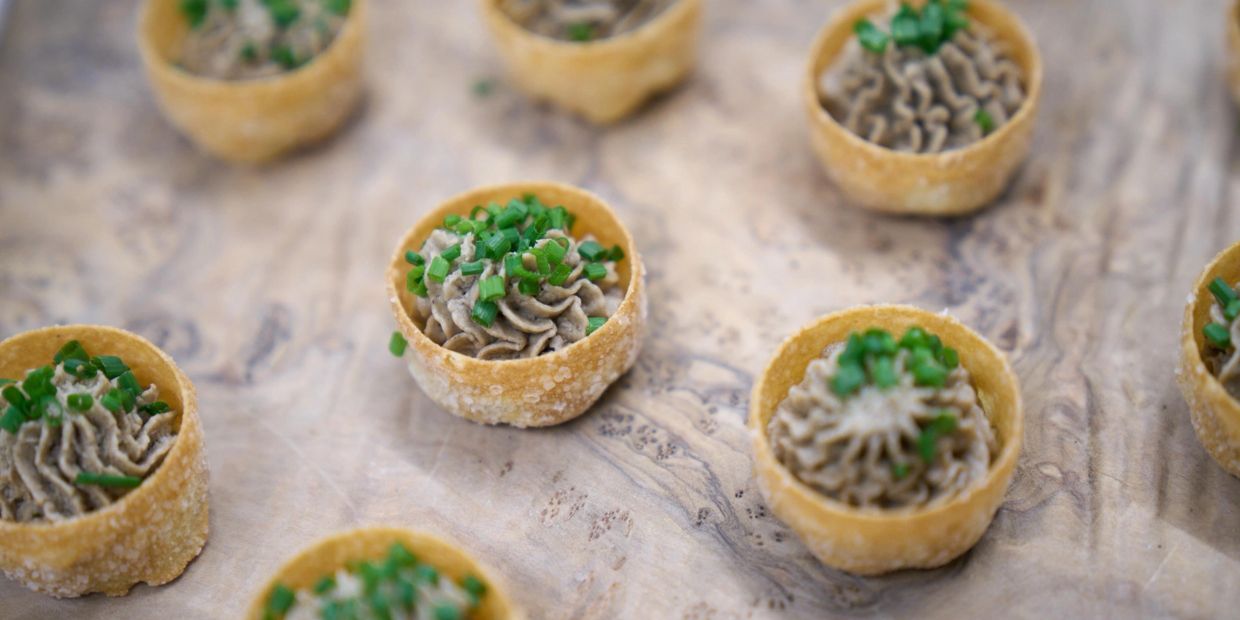 Mini tartlets filled with a creamy mixture and topped with chopped green herbs.