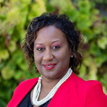 Professional woman smiling outdoors in a red blazer and pearl necklace.