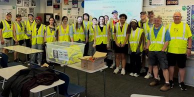 Group of students and adults in yellow safety vests in a classroom.
