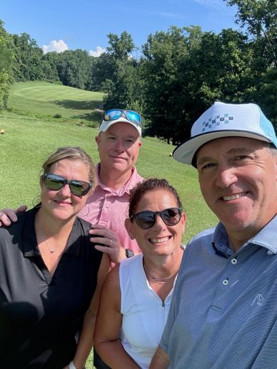 Four friends posing for a selfie on a sunny golf course.
