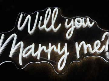 Neon sign glowing with the words 'Will you marry me?' in cursive.