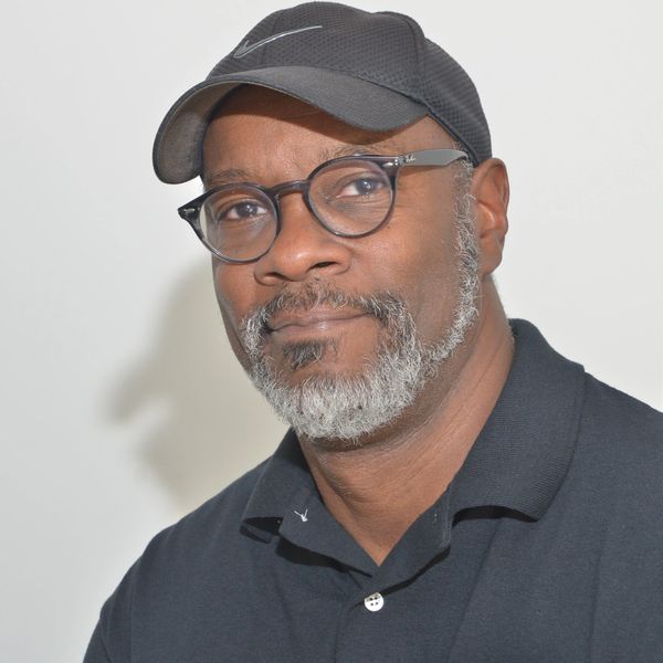 Man with glasses and gray beard wearing a black cap and polo shirt.