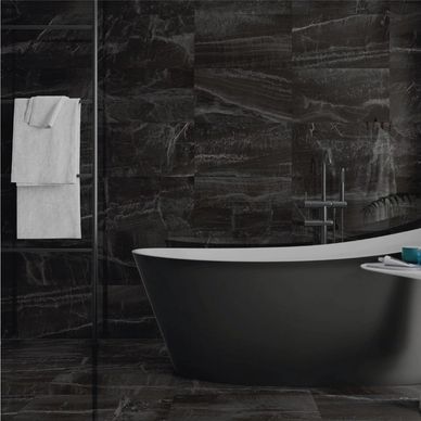 Modern black bathtub with white towels and toiletries in a dark marbled bathroom.