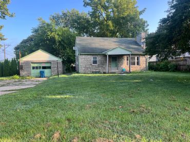 Small brick house with detached garage and large front yard.