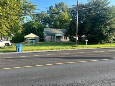 Old house with green garage and trees along the roadside.