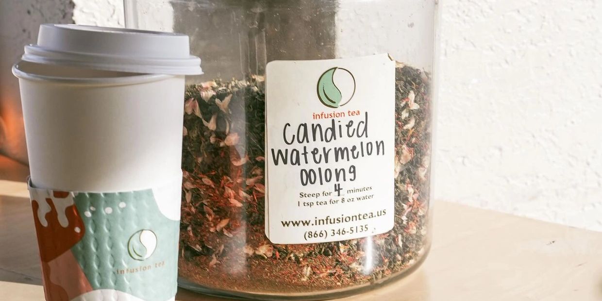 A cup of tea next to a jar of candied watermelon oolong tea leaves.