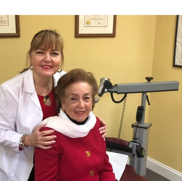 Doctor with elderly patient in medical office, both smiling warmly.