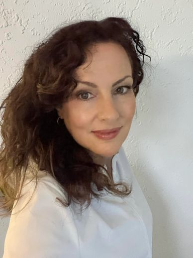 Woman with curly hair smiling softly in front of a textured white wall.