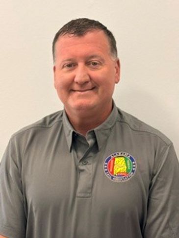 Man in a gray polo shirt with a colorful emblem smiling.