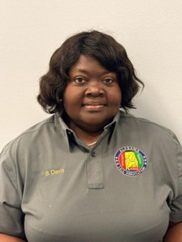 Woman in a gray uniform shirt with a name tag and emblem.
