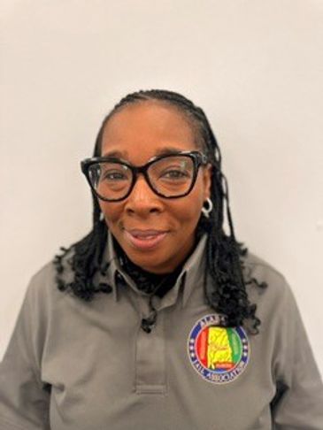 Woman with braided hair and glasses wearing a gray shirt with a colorful patch.