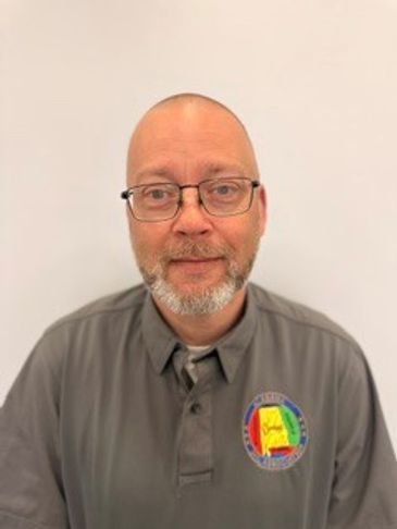 Man wearing glasses and a gray polo with a colorful patch.