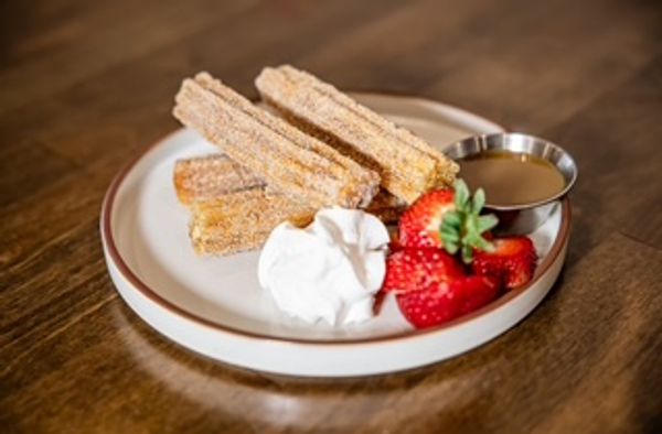 Plate of churros with whipped cream, strawberries, and caramel sauce.