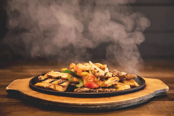 Sizzling grilled chicken fajitas with colorful bell peppers served on a wooden platter.
