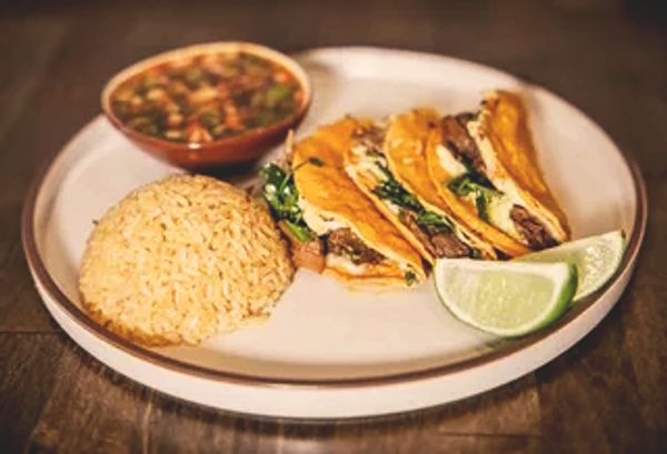 Plate with rice, three tacos, lime wedges, and a bowl of salsa.
