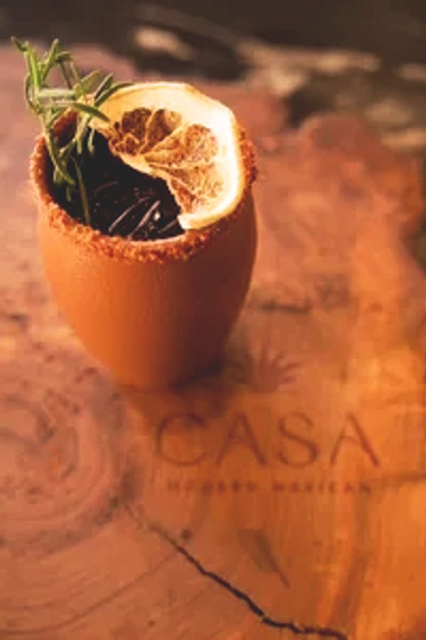 A cocktail garnished with a dried lemon slice and herbs on a wooden surface.