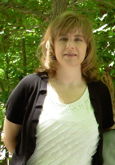 Woman standing outdoors with trees in the background.