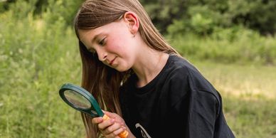 Girl looking through a magnifying glass down at the ground.