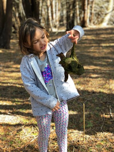 Young child holding up a moss covered piece of bark. Standing in a forest.