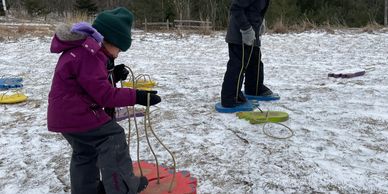Two children in winter coats and snow pants using large foam feet prints to make prints in snow