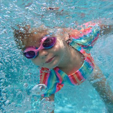 A child wearing colorful goggles swims underwater in a pool.