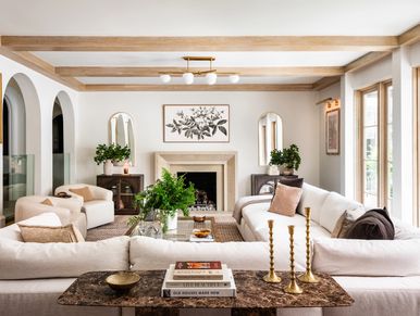 Bright transitional living room with white sectional sofas, a fireplace, wood ceiling beams, and arc