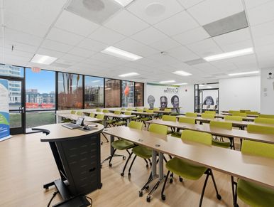 Modern classroom with rows of green chairs, training tables, a presentation podium, and large city-v