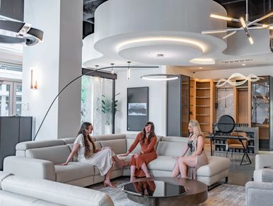 Three women seated in a bright modern lounge with curved sofas, contemporary lighting, and open shel