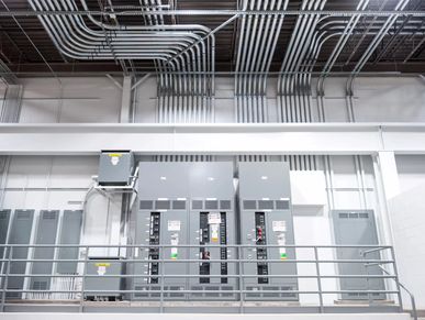Industrial electrical room with distribution panels and organized metal conduits running across the 