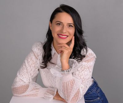 Smiling woman with dark hair in a white lace blouse and jeans.
