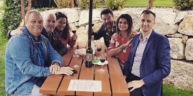 a group of people sitting at a picnic table drinking wine